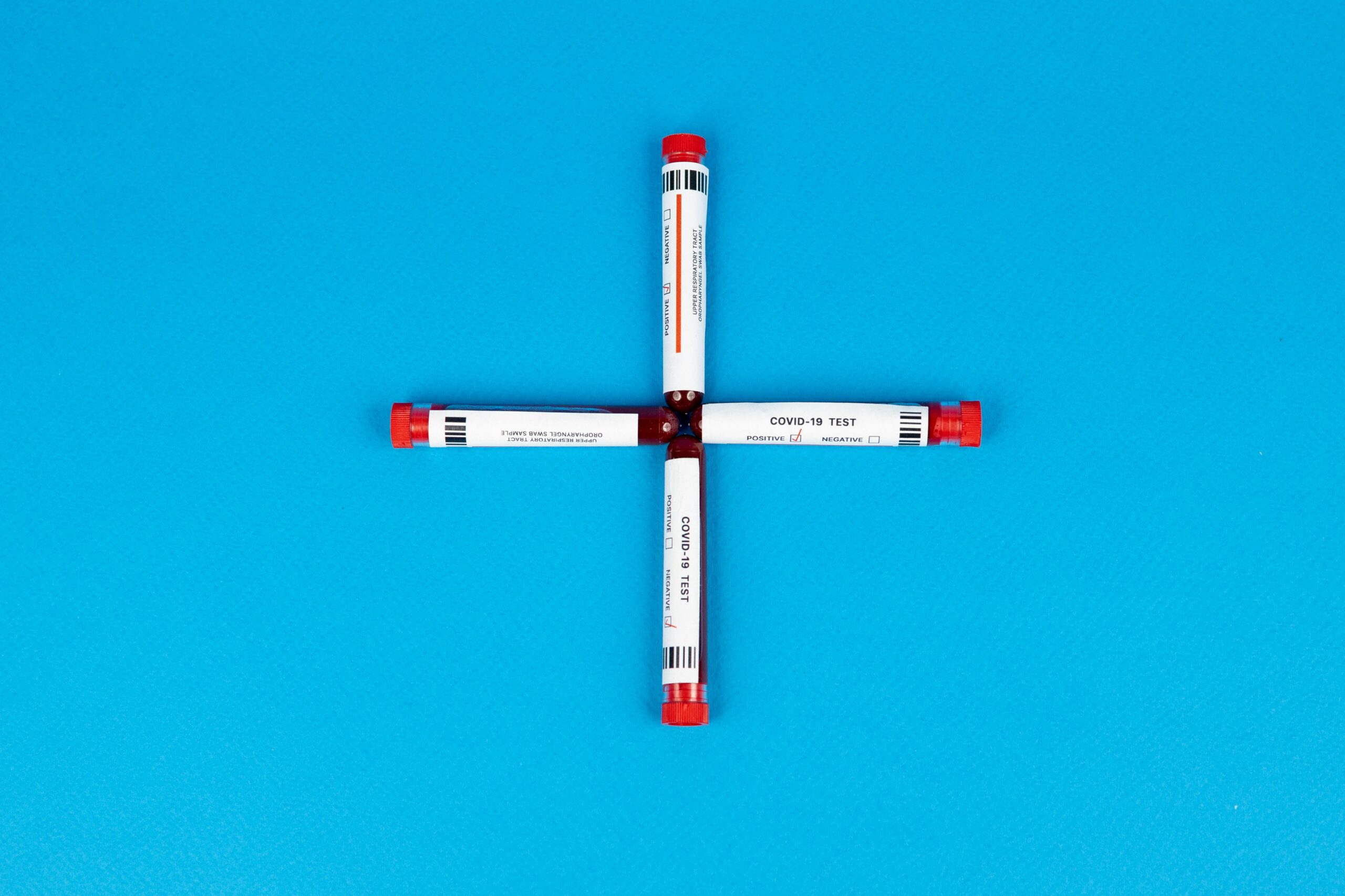 Four COVID-19 test tubes arranged in a cross shape on a vivid blue background.